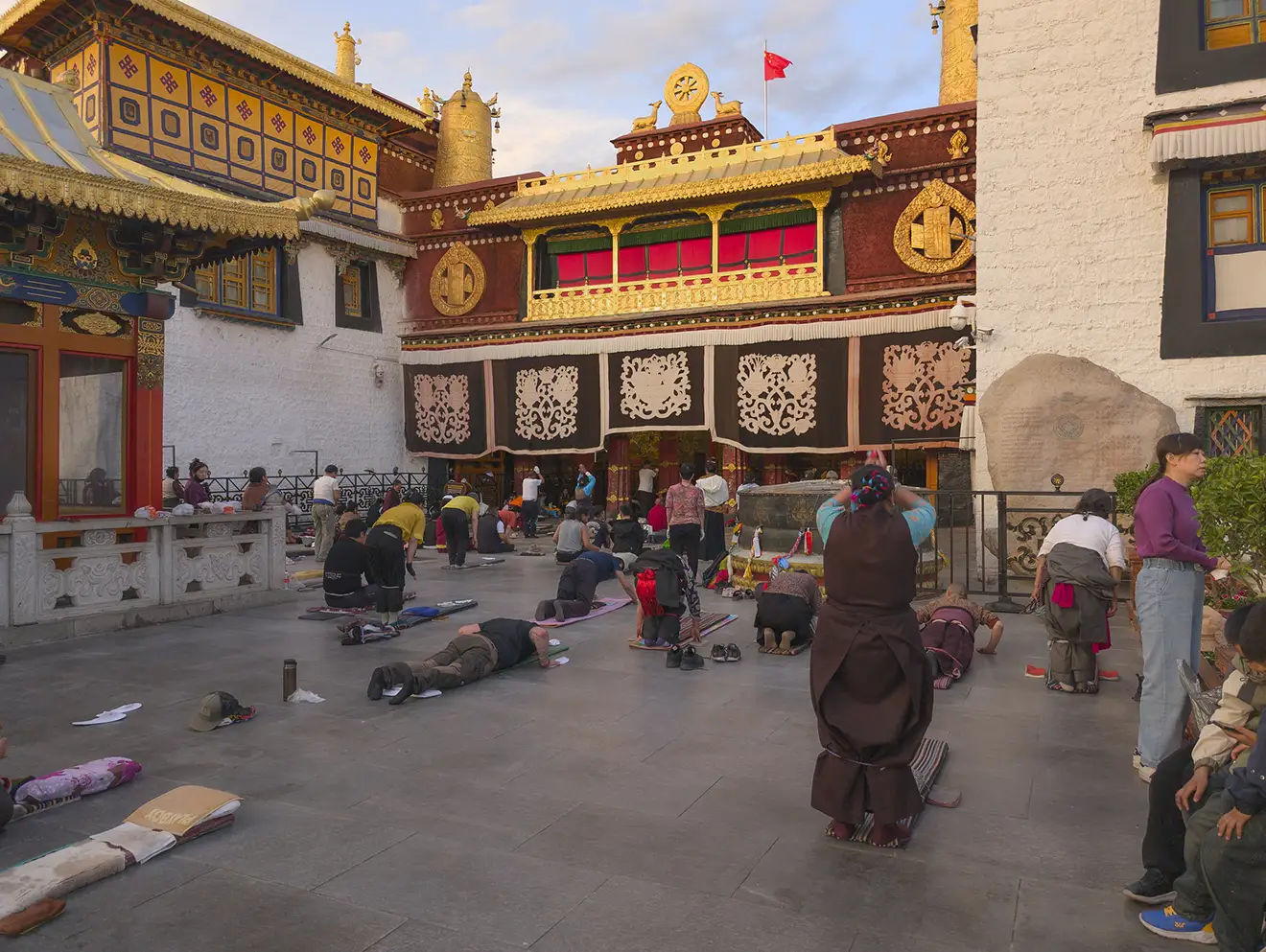 Pilgrims perform full-body prostrations at Jokhang Temple in Lhasa during the Lhasa to Everest Base Camp and Namtso Lake Tour, surrounded by traditional Tibetan architecture and prayer spaces.