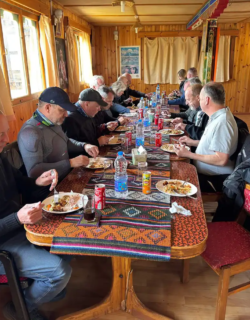 A group of adventure riders enjoys a traditional meal at a long wooden table inside a cozy Bhutanese restaurant during a Bhutan motorcycle tour.