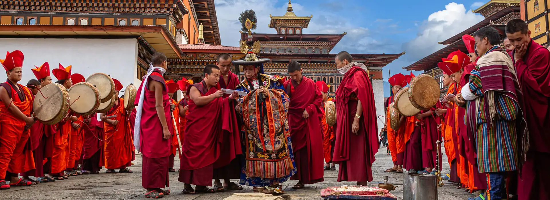Monks in red robes play traditional drums and perform sacred rituals during a Tsechu festival, a vibrant highlight of a Bhutan Cultural Tour.