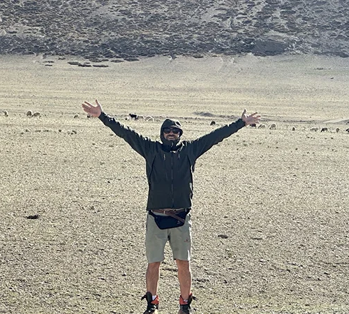 A male hiker raises his arms in a high-altitude Tibetan valley. Check our detailed Tibet packing list for suggestions on quality windproof jackets and sun protection for this rugged environment.