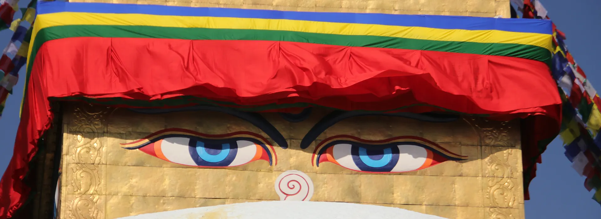 The iconic wisdom eyes of Boudhanath Stupa are painted on a golden spire under colorful prayer flags, representing the best short trips in Nepal.