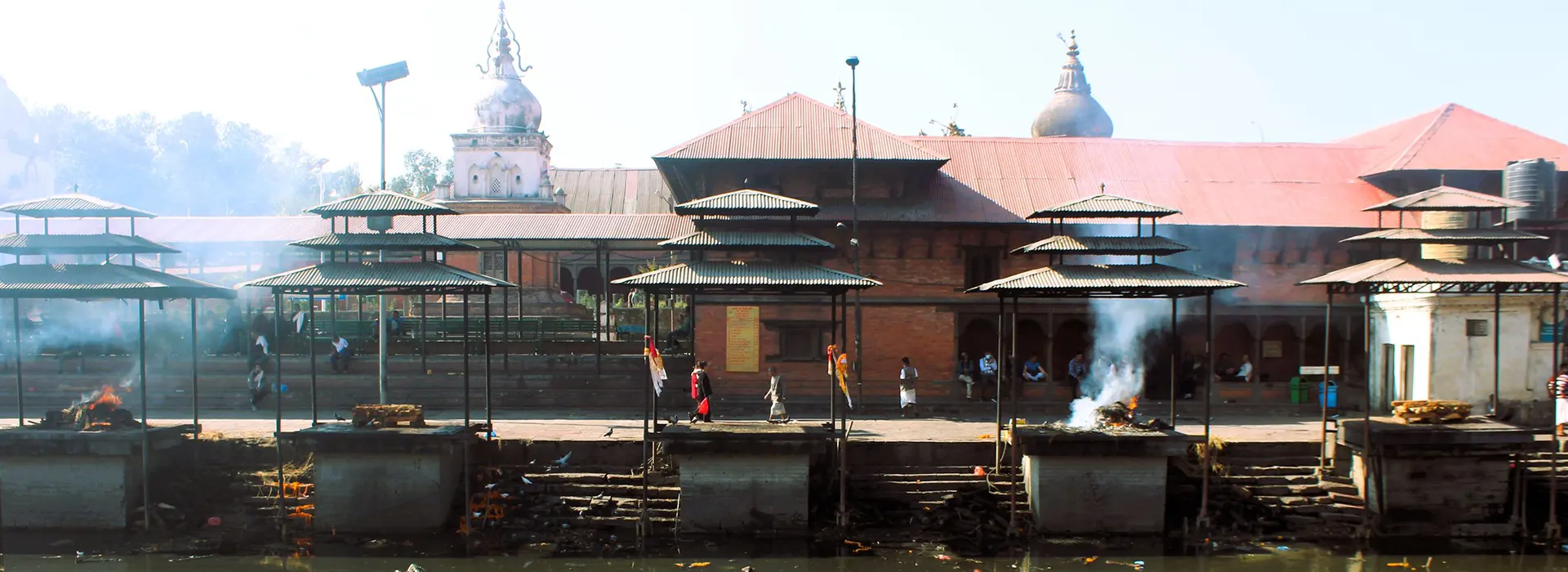 A panoramic view of the sacred Bagmati River banks at Pashupatinath Temple, one of the best cultural destinations in Nepal, showing traditional funeral pyres and shrines.