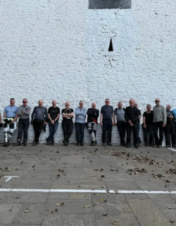 A large group of adventure riders and their local guide pose against a high white stone wall during a Bhutan motorcycle tour.