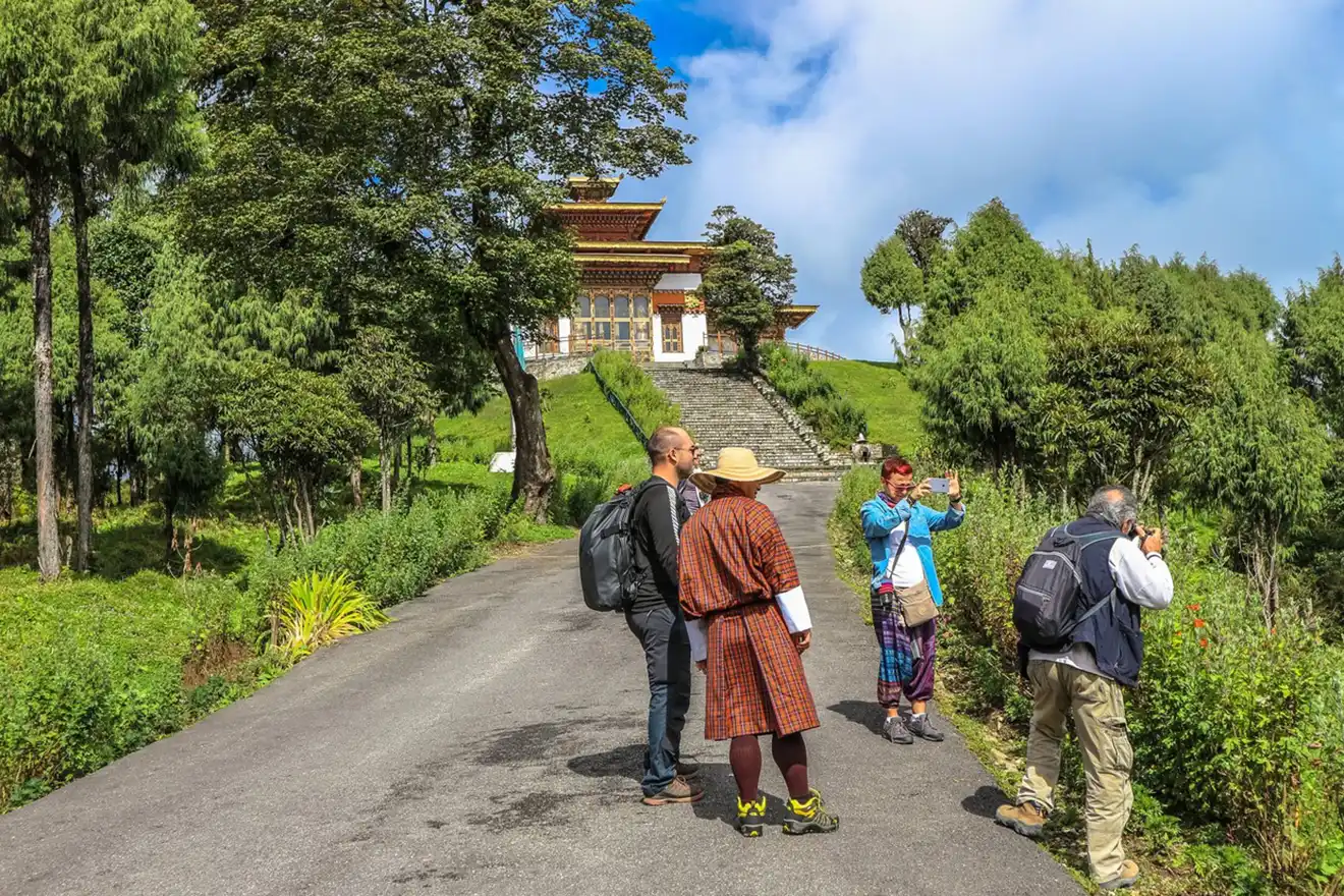 A group of tourists and a local guide in traditional dress explore a hillside temple garden during an immersive Bhutan Botanical Tour.
