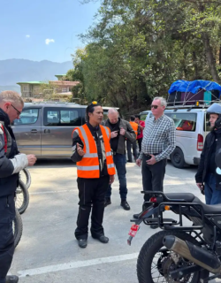 A tour guide in a safety vest briefs a group of riders next to their bikes before starting a daily leg of a Bhutan motorcycle tour.