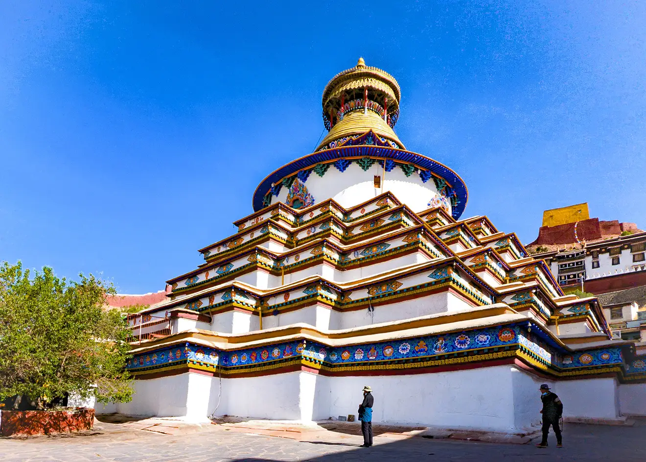 Colorful Kumbum Stupa at Gyantse Monastery under a clear blue sky during the Lhasa to Everest Base Camp and Namtso Lake Tour, with traditional Tibetan design and visitors nearby.