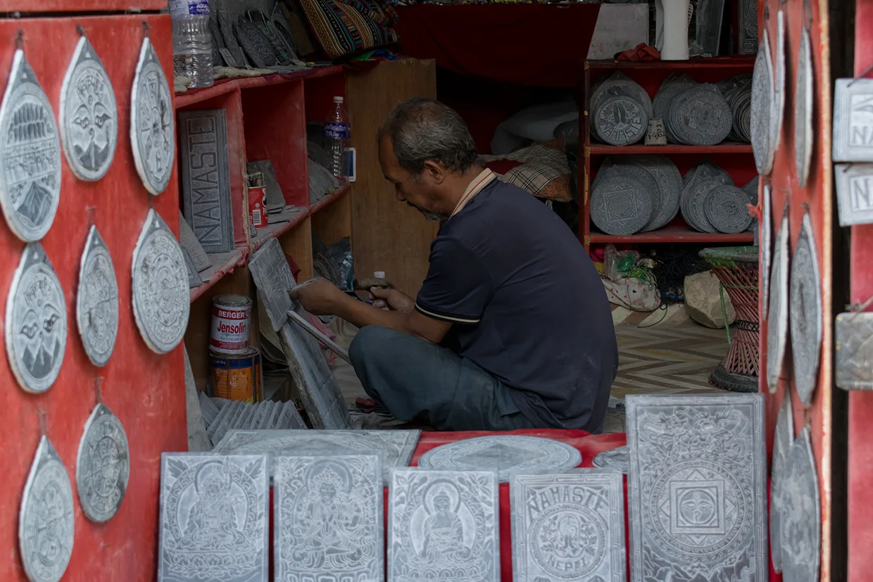 A local artisan carves intricate designs into stone slabs in a small workshop. These handmade souvenirs are a cultural highlight found in any Kathmandu Travel Guide.