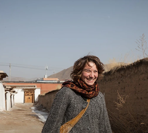 A smiling female traveler walks through a traditional village street. Understanding Tibet Tour Requirements helps visitors enjoy a seamless experience while exploring these historic local neighborhoods.