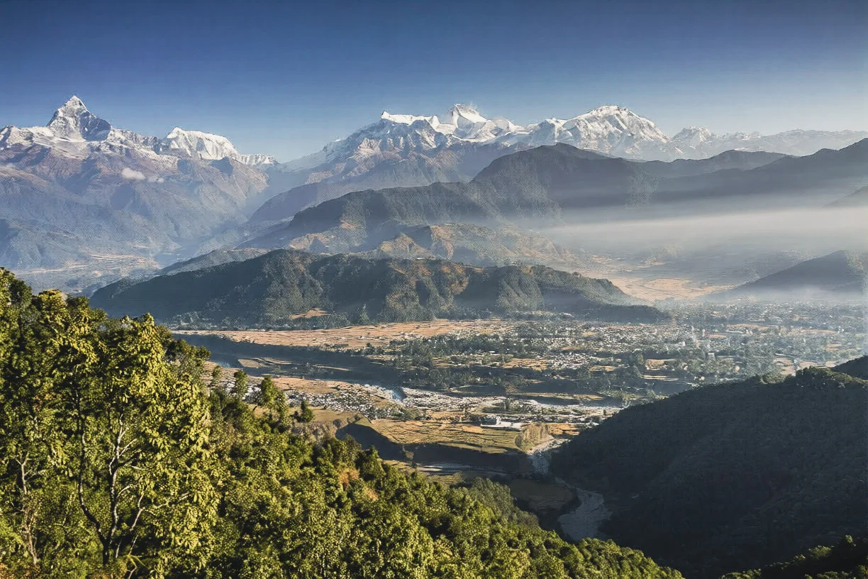 A wide panoramic photograph from Sarangkot shows multiple paragliders soaring high above a mountain range, overlooking a valley and Phewa Lake, perfect for finding the best places to visit in Pokhara.