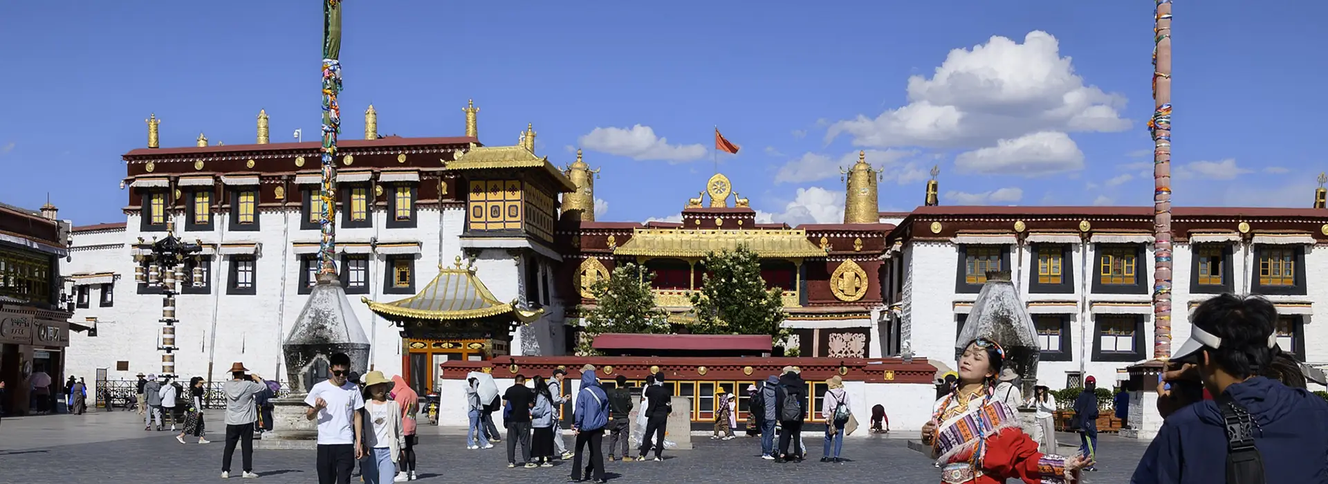 Tourists explore the Jokhang Temple square, a major starting point for the Lhasa to Kathmandu Overland Tour, under a clear blue sky with white clouds.