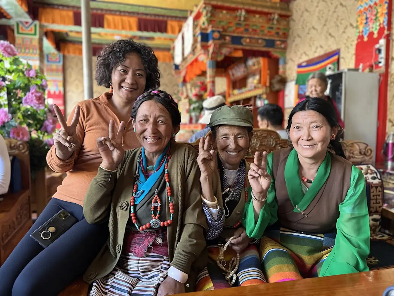 Four local women smile and pose inside a colorful traditional teahouse. Access to these remote cultural hubs often requires travelers to hold a valid Tibet Military Permit.