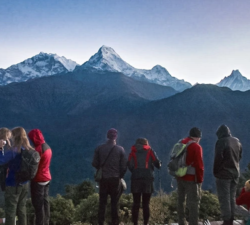 A group of hikers in colorful jackets gazes at the snow-capped Himalayan peaks during sunrise, a scene every traveler should prepare for using a Nepal Hiking Packing List.