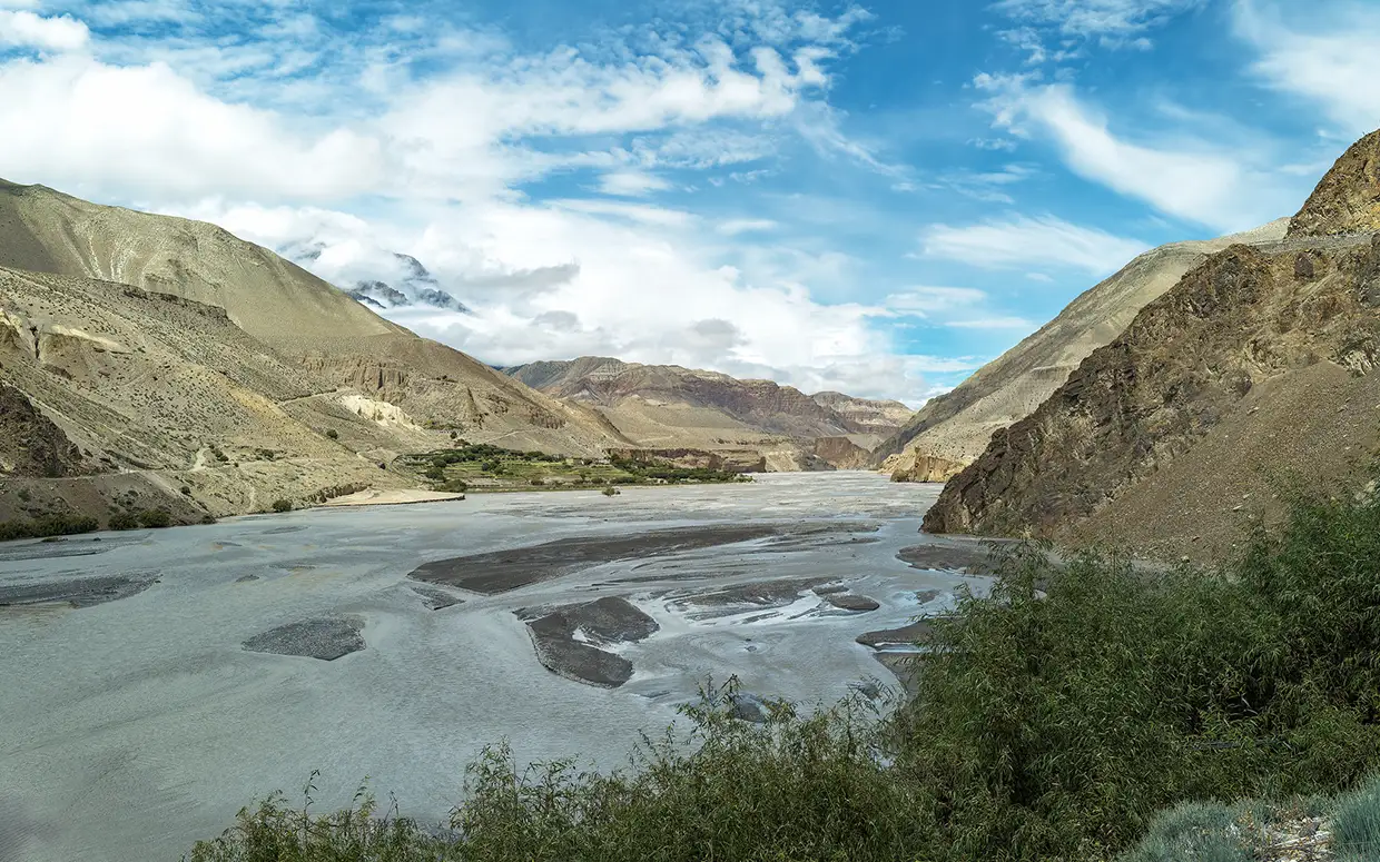 The wide, grey Kali Gandaki River flows through the arid Mustang valley, a rain-shadow region that stays dry during the monsoon, as noted in various Nepal weather by month guides.