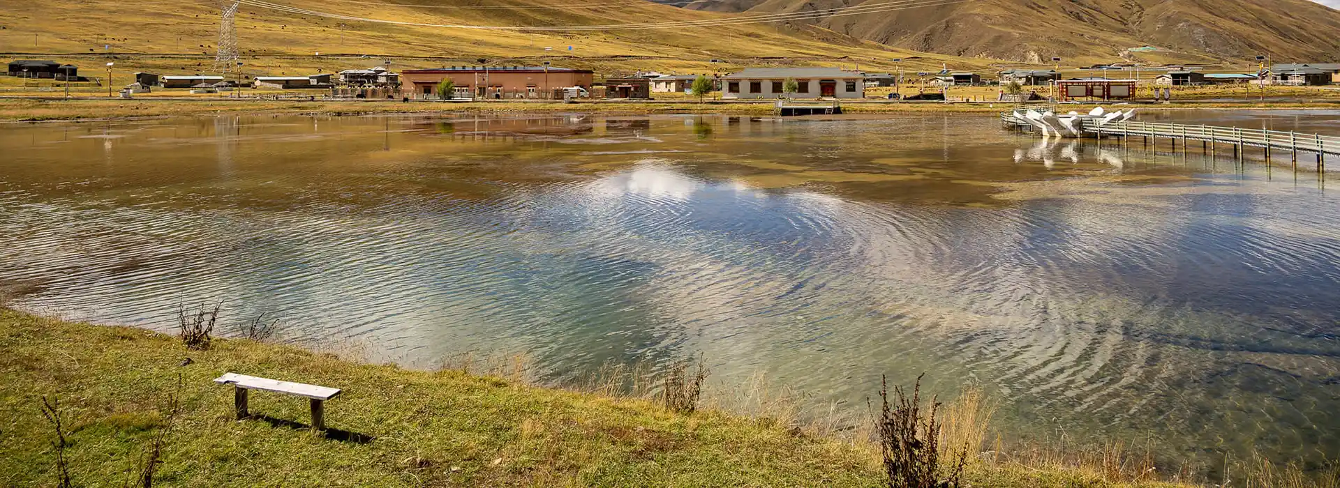 A serene Tibetan lake reflects the golden sunlight near a small village. Travelers must navigate the Tibet visa process in Kathmandu to witness these stunning landscapes.