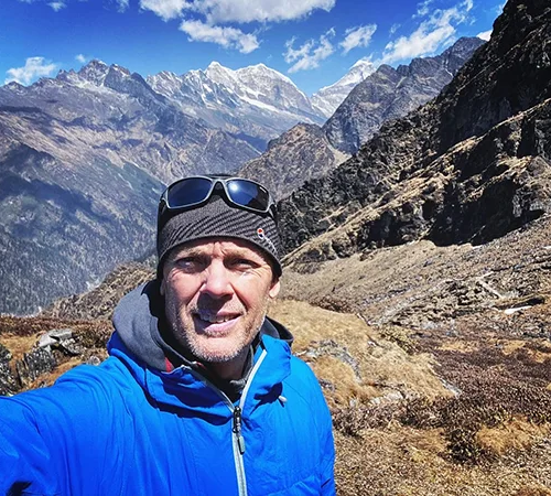 A smiling adventurer takes a selfie during a high-altitude trek, featuring towering snow-capped peaks and vast valleys, illustrating active things to do in Nepal.