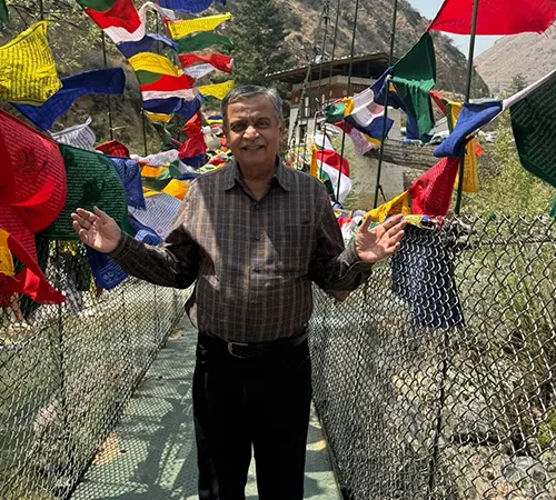 A man walks across the longest suspension bridge in Punakha while colorful prayer flags flutter in the wind on a Bhutan Golden Triangle Tour.