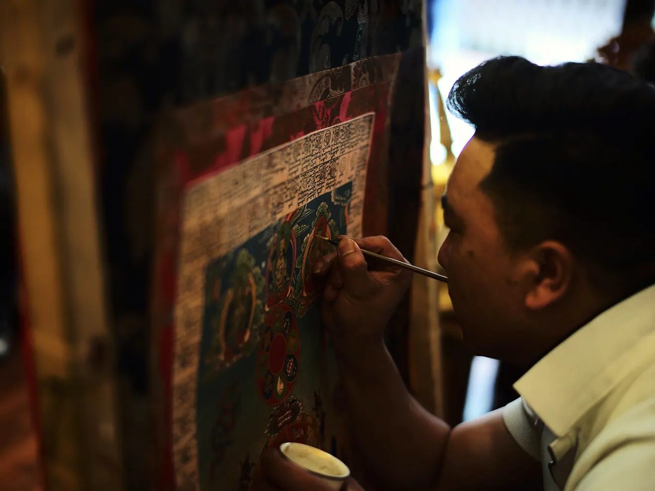 A master artist carefully paints intricate details onto a large traditional thangka painting in Lhasa. These exquisite artworks are a prime option for what to buy in Tibet.