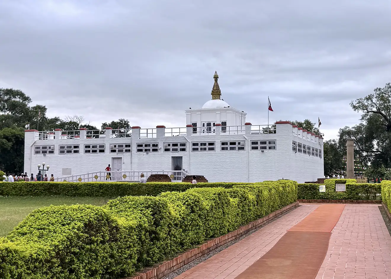 The white Maya Devi Temple stands behind green hedges and a brick walkway. This sacred birthplace of Buddha is a spiritual stop on a 2-week Nepal itinerary.
