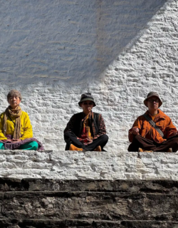 Three travelers sit in meditation pose on a whitewashed ledge, backlit by strong sun, finding stillness during a reflective Phobjikha Valley Nature Tour.