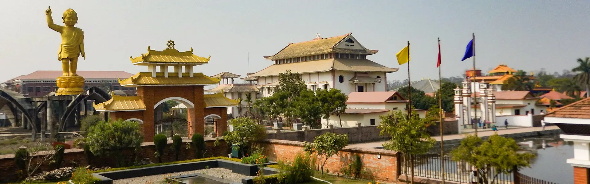 A golden statue of the baby Buddha stands near a traditional gateway and temple buildings. This peaceful monastic site is one of the best places to visit in Lumbini.