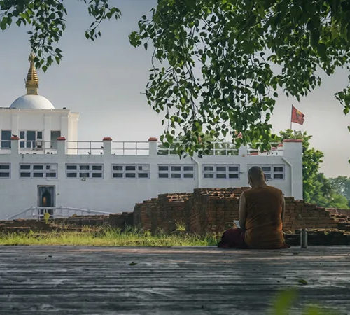 A monk sits peacefully in study before the white Maya Devi Temple and ancient brick ruins. This site is among the best places to visit in Lumbini.