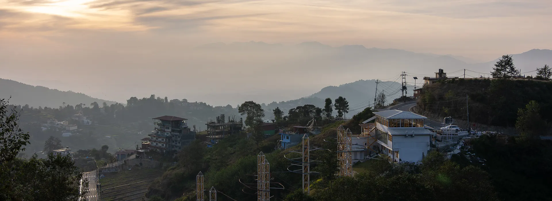 A panoramic morning view of a misty hillside town with buildings and distant mountains, showcasing the serene landscapes near the best cities to visit in Nepal.