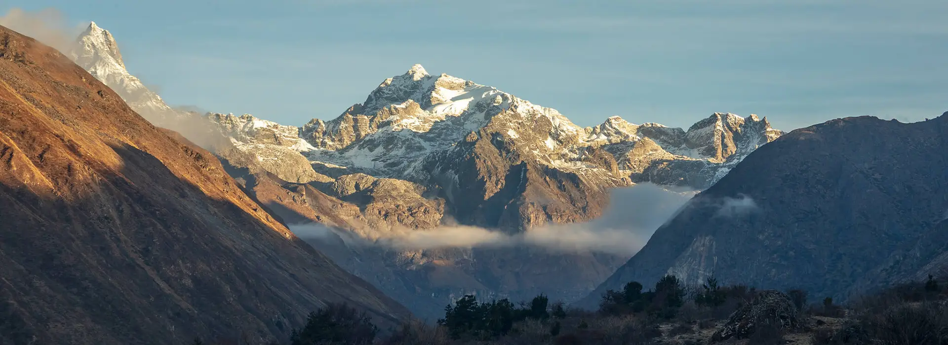 Snowy mountain peaks rise above a layer of clouds under a clear blue sky, capturing the rugged Himalayan scenery found along the Druk Path Trek.