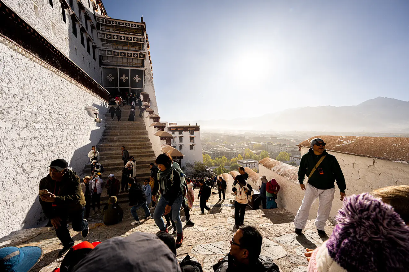A crowd of travelers ascends the historic stone steps of the Potala Palace in Lhasa. Proper documentation, like an Alien's Travel Permit, is necessary for visiting such locations in Tibet.