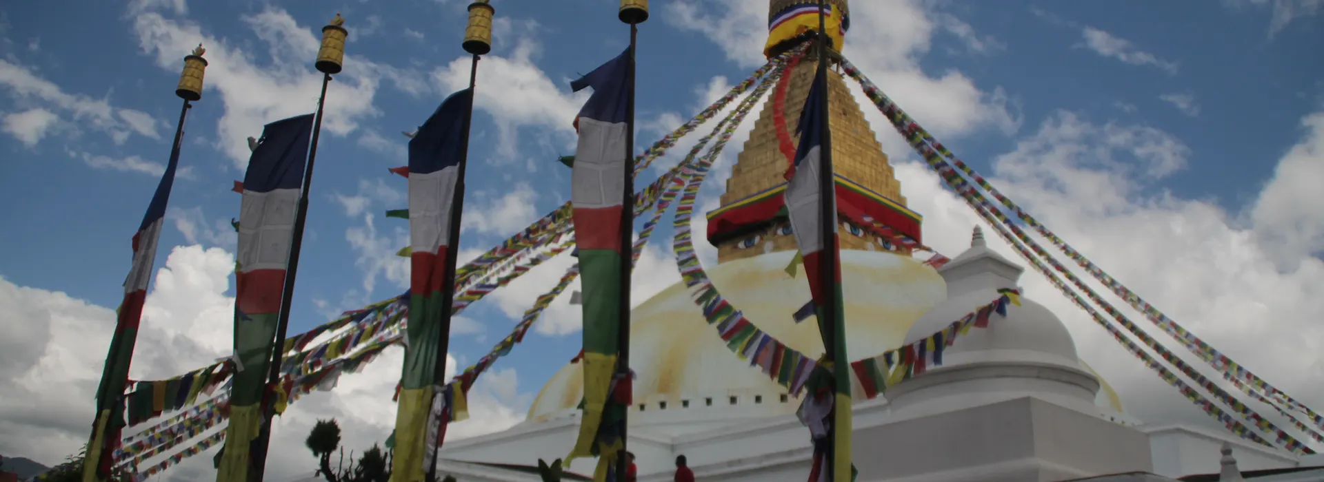 The magnificent Boudhanath Stupa stands in Kathmandu under a bright blue sky filled with clouds. Planning your visit to this UNESCO site requires checking the Nepal Weather by Month.