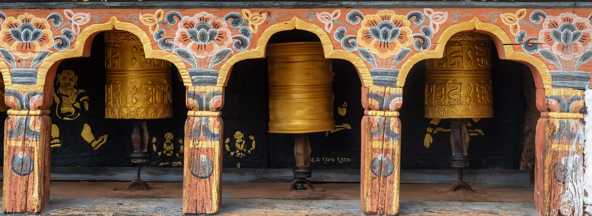 Ornate golden prayer wheels in a painted wooden frame at a monastery along the scenic Jomolhari Base Camp Trek in the Bhutanese Himalayas.