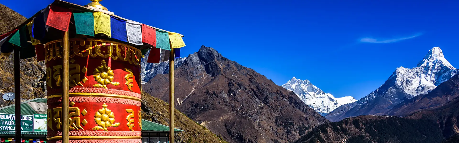 Vibrant Buddhist prayer wheels and colorful flags stand before the majestic, snow-capped Ama Dablam peak, a highlight for those following a Nepal Hiking Packing List.