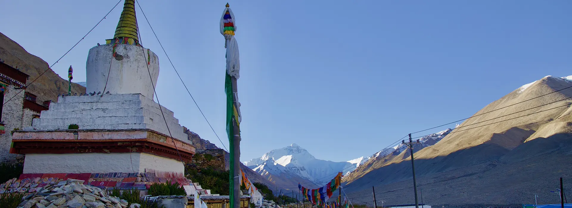 Buddhist stupa with prayer flags near Rongbuk Monastery, set against Himalayan peaks on the Lhasa to Everest Base Camp Tour route under a clear blue sky.