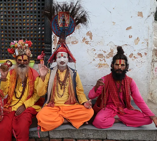 Three colorful Sadhus, holy men, in traditional dress sit outside a Nepali temple. Learning about local customs is a meaningful part of any Nepal Trip Cost calculation.