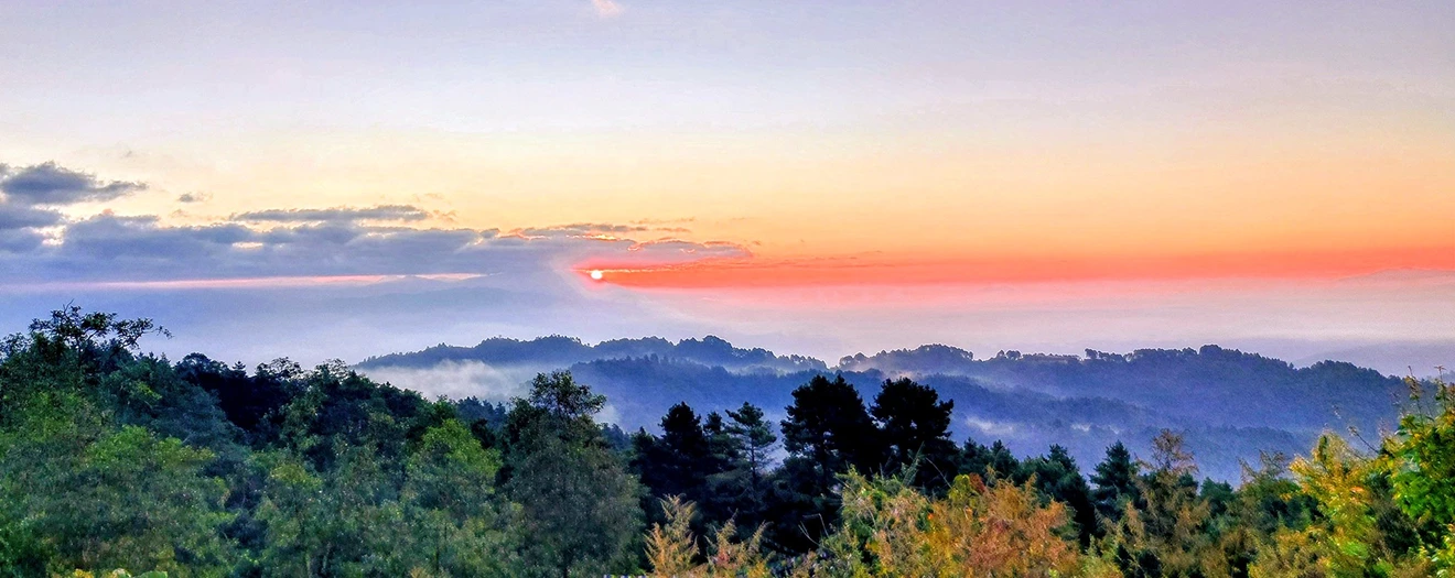 A golden sun rises over lush green hills and misty valleys in Pokhara, showcasing the natural beauty found on a Nepal Itinerary for 2 Weeks.