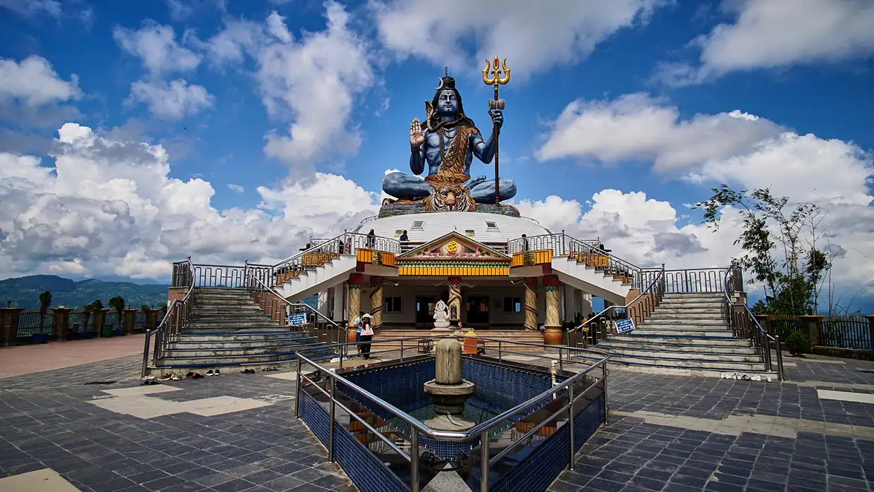A massive blue statue of Lord Shiva sits atop a white dome structure under a cloudy blue sky, representing the best places to visit in Pokhara.