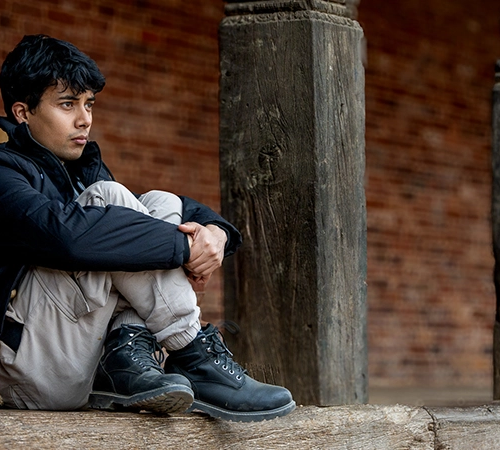 A traveler sits between ancient wooden pillars at a historic palace. Understanding Nepal entry requirements for tourists ensures a smooth start to your cultural journey.