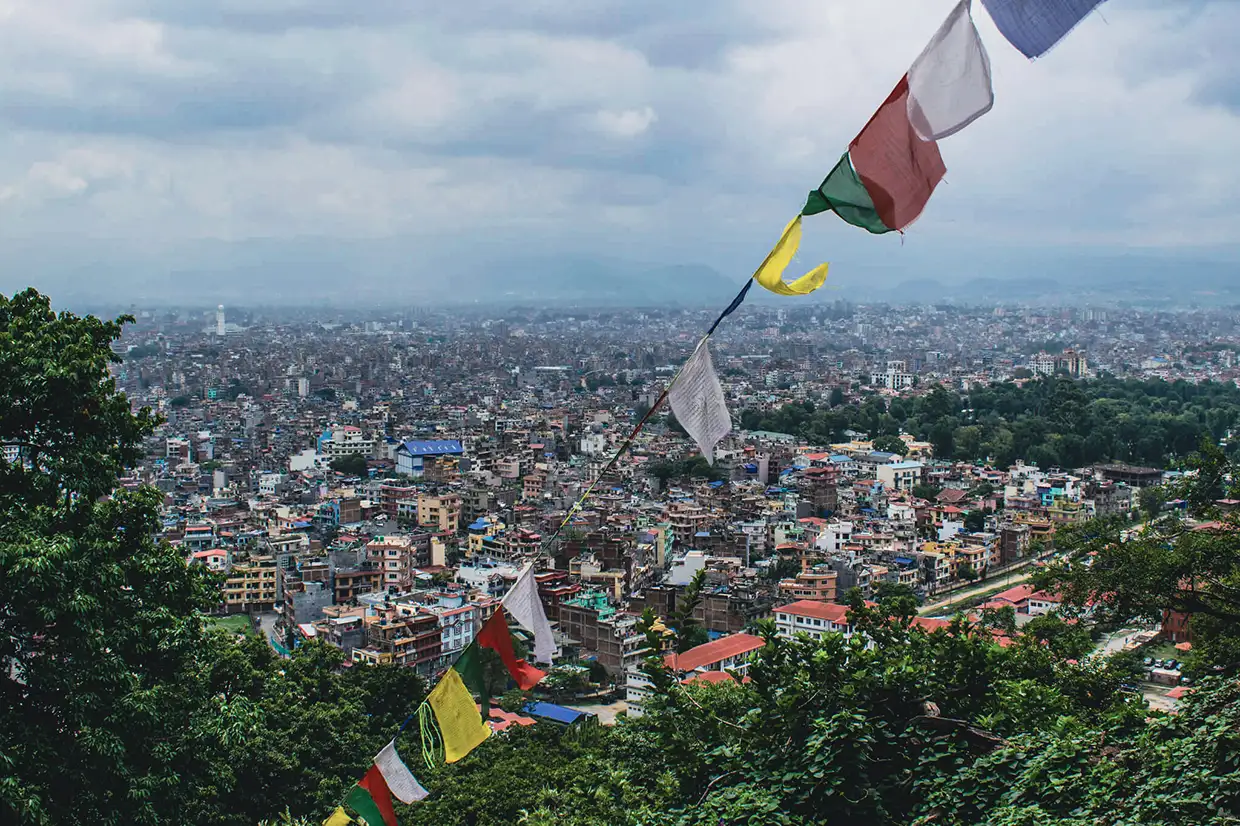 Colorful Buddhist prayer flags hang over a panoramic view of the dense Kathmandu Valley skyline. This famous viewpoint is a centerpiece of any Kathmandu Travel Guide.