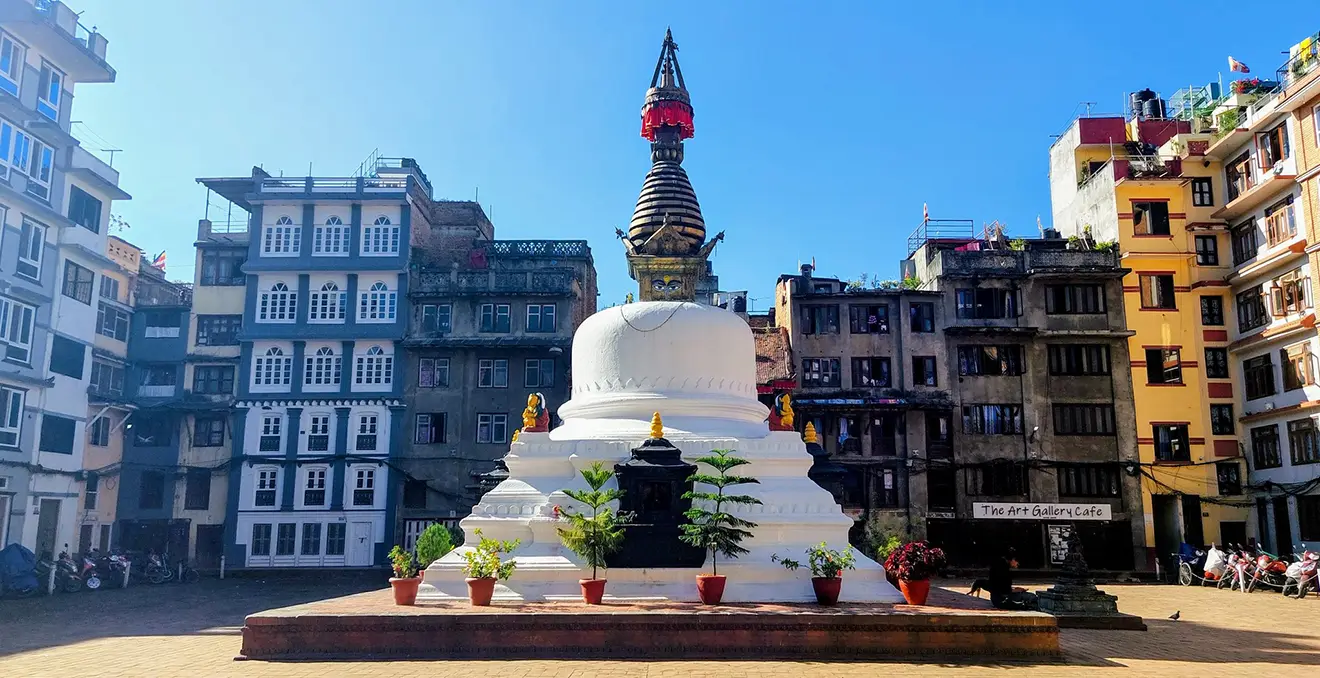 A white Buddhist stupa with a red finial sits in a Kathmandu square, surrounded by multi-story traditional Nepalese buildings, a key cultural sight to include in a Nepal Itinerary for 2 Weeks.