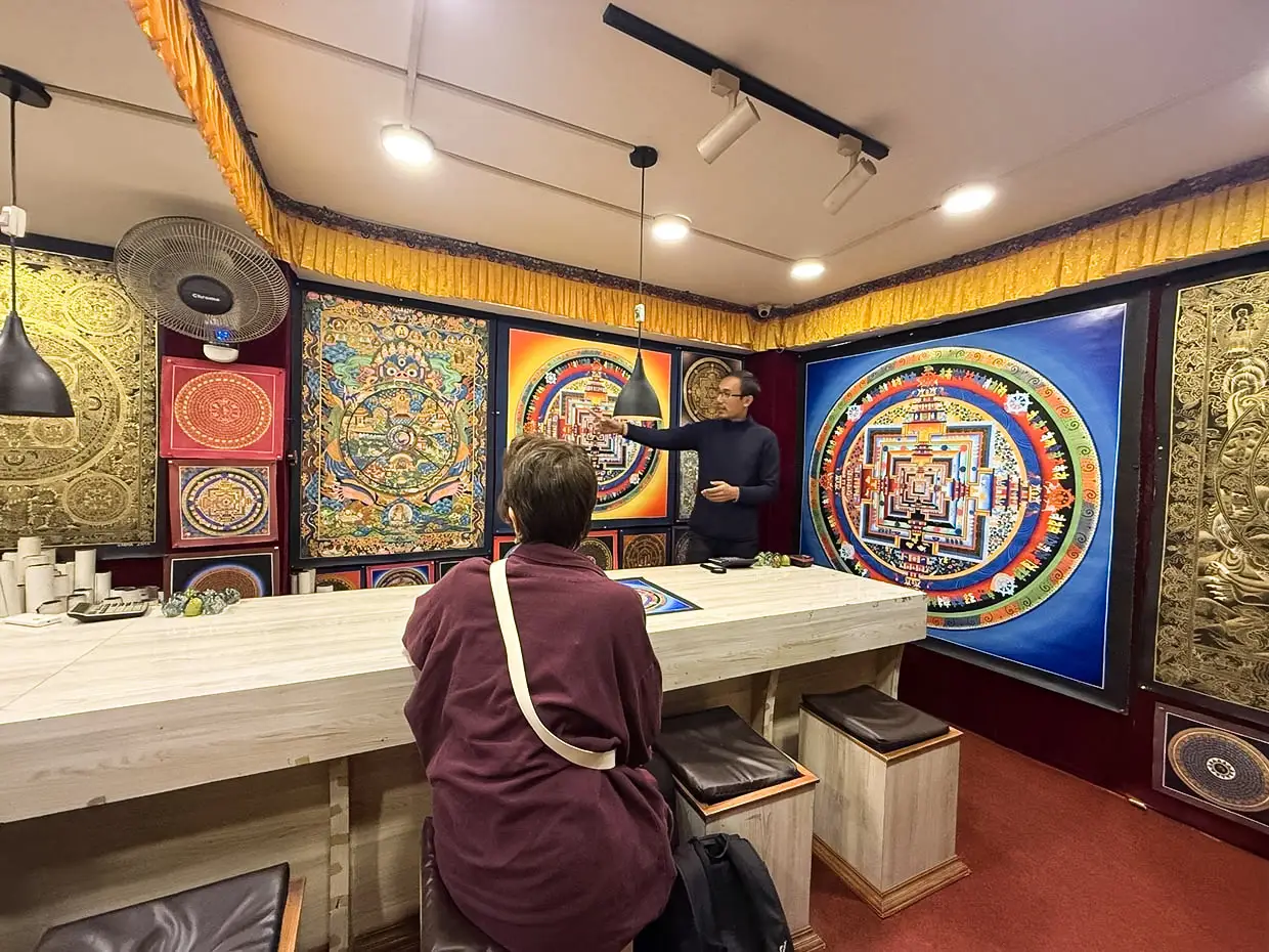 A man explains a large, colorful, circular Kalachakra thangka painting to a visitor inside a Nepalese art gallery, showcasing culturally enriching things to do in Kathmandu.
