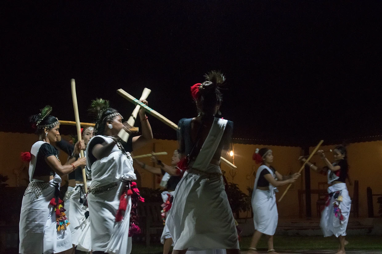 Local Tharu people perform a traditional stick dance in white and black traditional attire under the dark night sky. This is one of the unique cultural things to do in Chitwan.