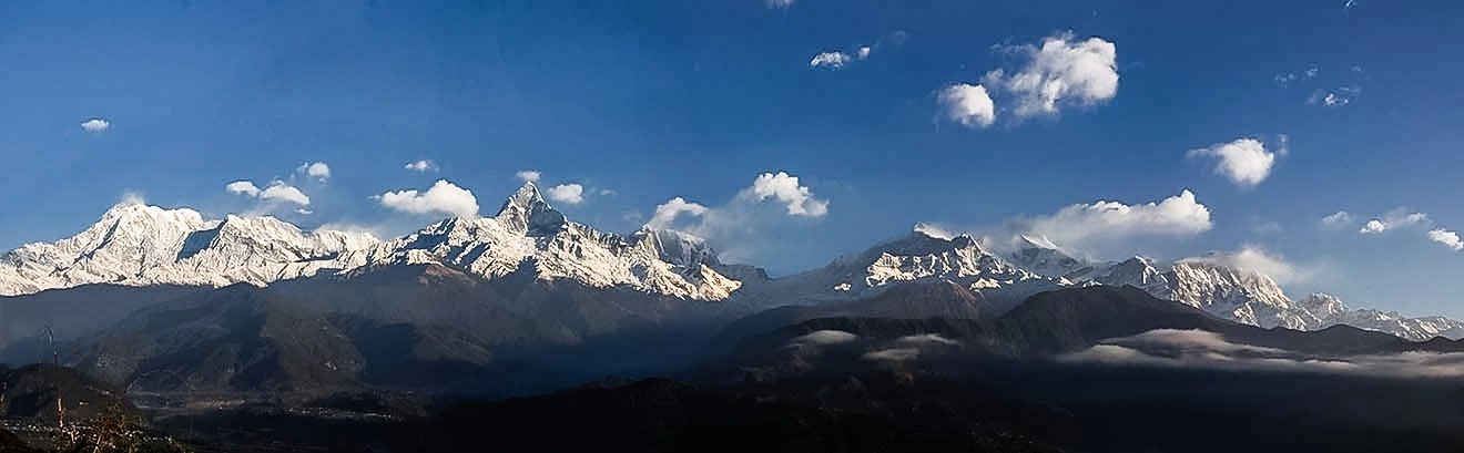 The massive, snow-capped Annapurna mountain range is seen against a blue sky, a view rare during the peak monsoon season described in any Nepal weather by month guide.