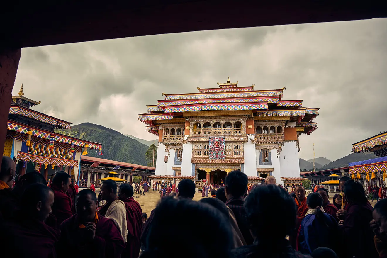 A crowd of locals and monks gathers in the courtyard of the ornate Gangtey Monastery during a traditional festival on a Bumthang Cultural Trek and Tour.