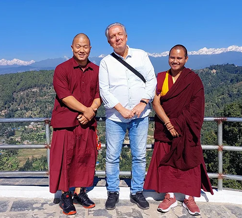 A traveler in a white shirt stands with two Buddhist monks against a stunning backdrop of the Himalayan mountains, a highlight for a 10-Day Nepal Itinerary.