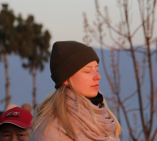 A woman wearing a beanie and scarf enjoys the morning warmth in Nagarkot. This peaceful sunrise view is a highlight of the best short trips in Nepal.