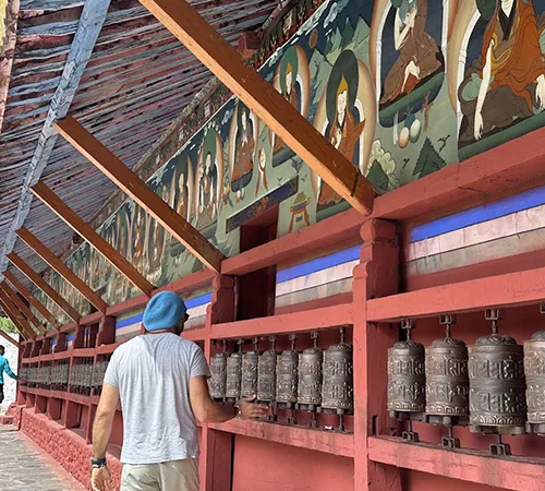 A traveler in a blue beanie turns prayer wheels at a Tibetan monastery, experiencing spiritual sites during a scenic Kathmandu to Lhasa Tour across the Himalayas.