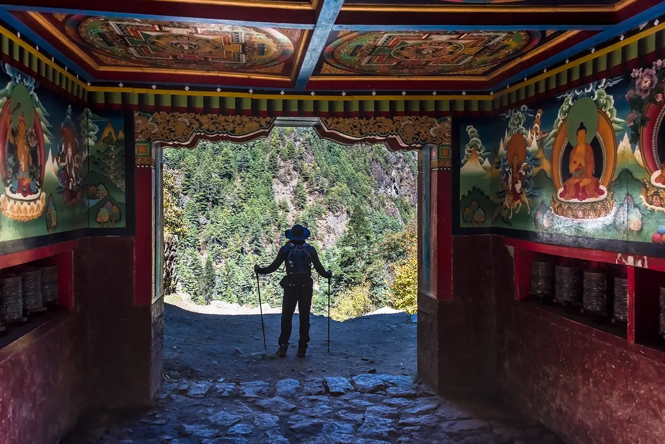 A smiling female trekker stands on a mountain trail, holding trekking poles and looking at a snow-capped peak in one of the best mountain destinations in Nepal.