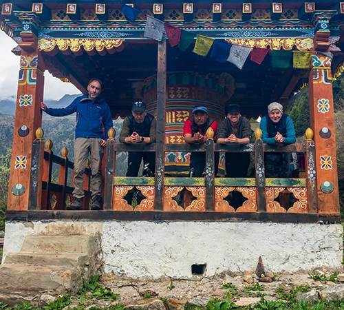 Five hikers stand within a traditional wooden structure featuring a large prayer wheel during their journey on the Druk Path Trek in Bhutan.