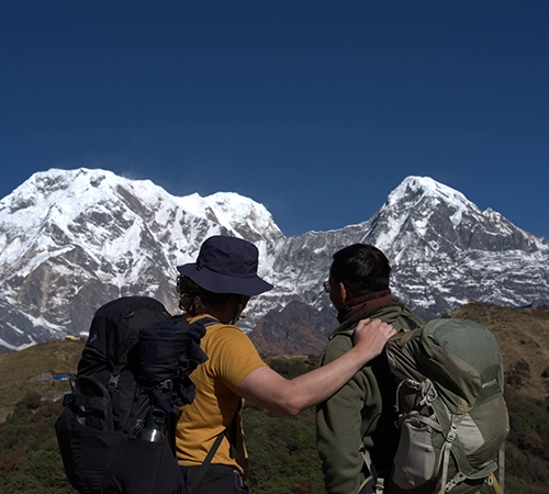 Two well-equipped hikers with backpacks gaze towards massive snow-covered peaks, highlighting the incredible trekking available in the best mountain destinations in Nepal.