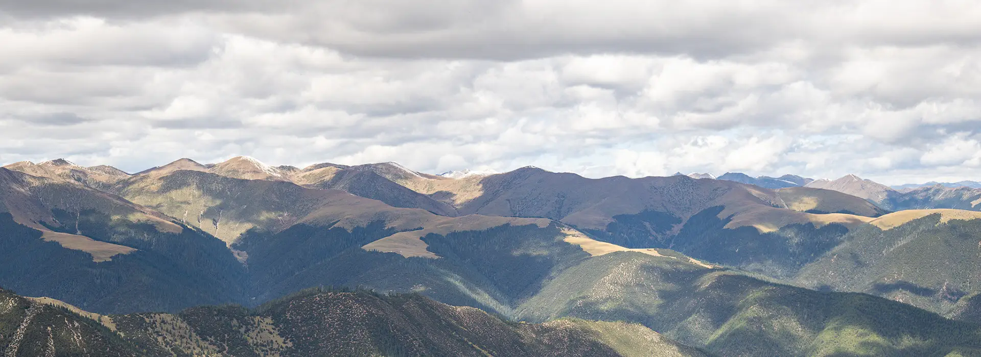 An aerial panoramic photograph of rugged, sun-dappled mountains near a traditional trade route, where travelers decide what to buy in Tibet to bring home.