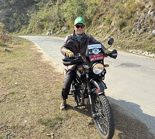 A man rides a motorcycle on a winding mountain road decorated with red prayer flags during a Bhutan Motorcycle Tour.